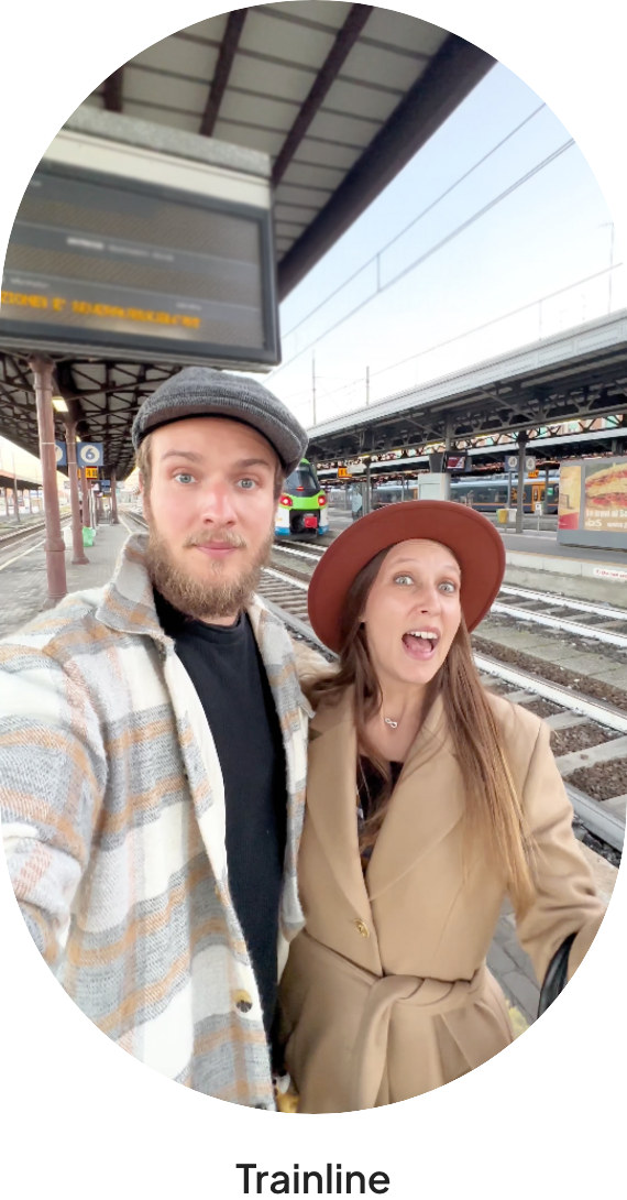 Oval photo from a 40Degrees campaign: two creators in hats take a selfie on a railway platform under the station roof, with the caption Trainline