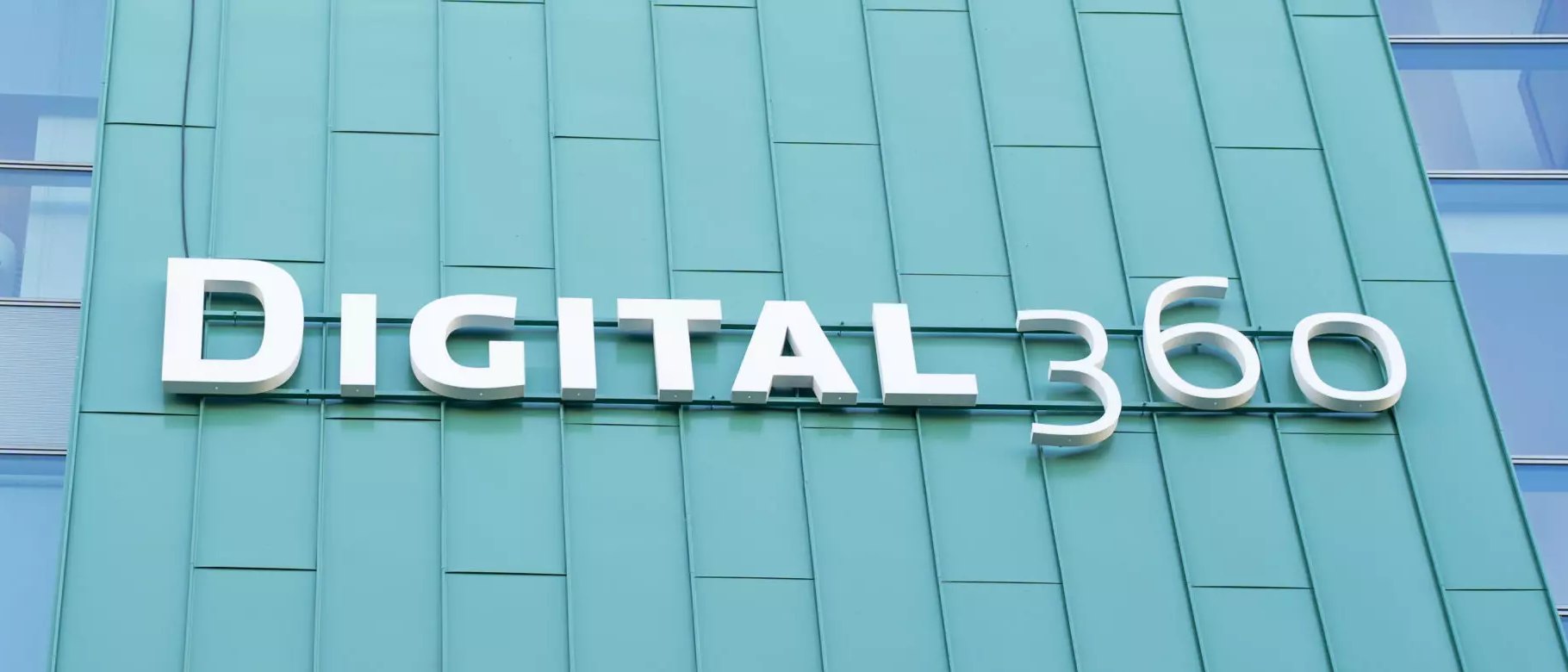 White Digital360 lettering on the teal-green panelled facade of the group's office building, seen from below, with glass windows at both edges