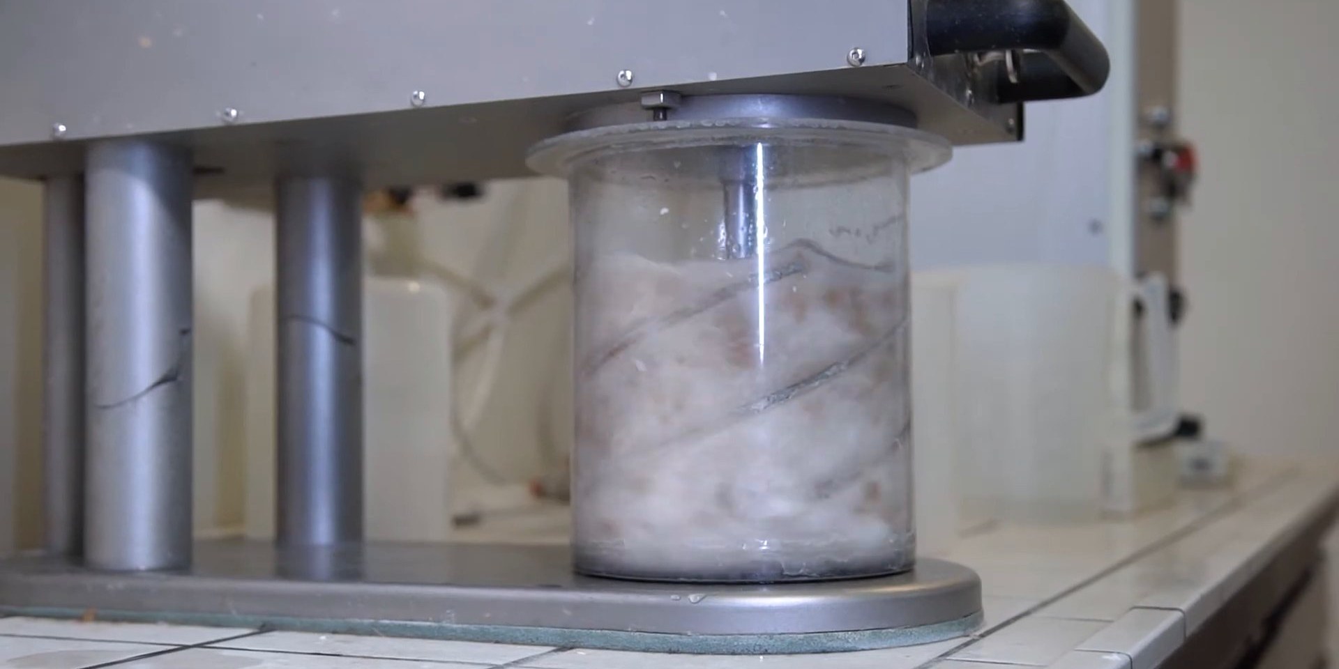 Clear laboratory disintegrator vessel full of swirling paper pulp under a steel motor head